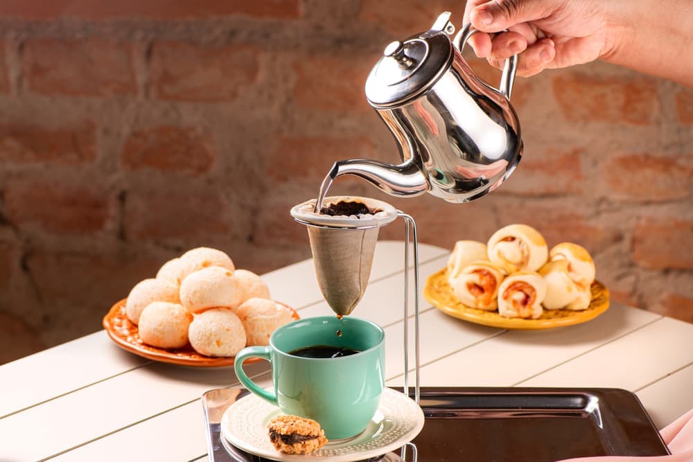 Café sendo servido na xícara verde, com enroladinhos.