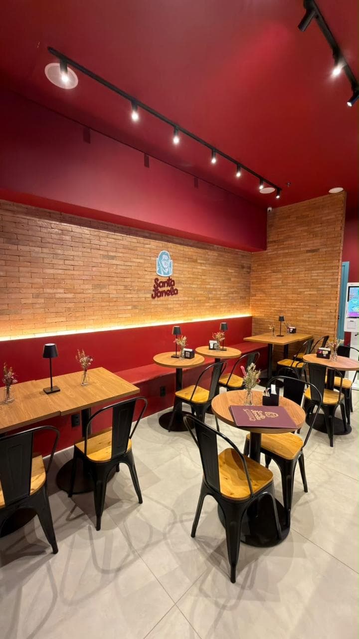 O salão da unidade café: parede de tijolinho, teto vermelho e mesas de madeira com cadeiras pretas.